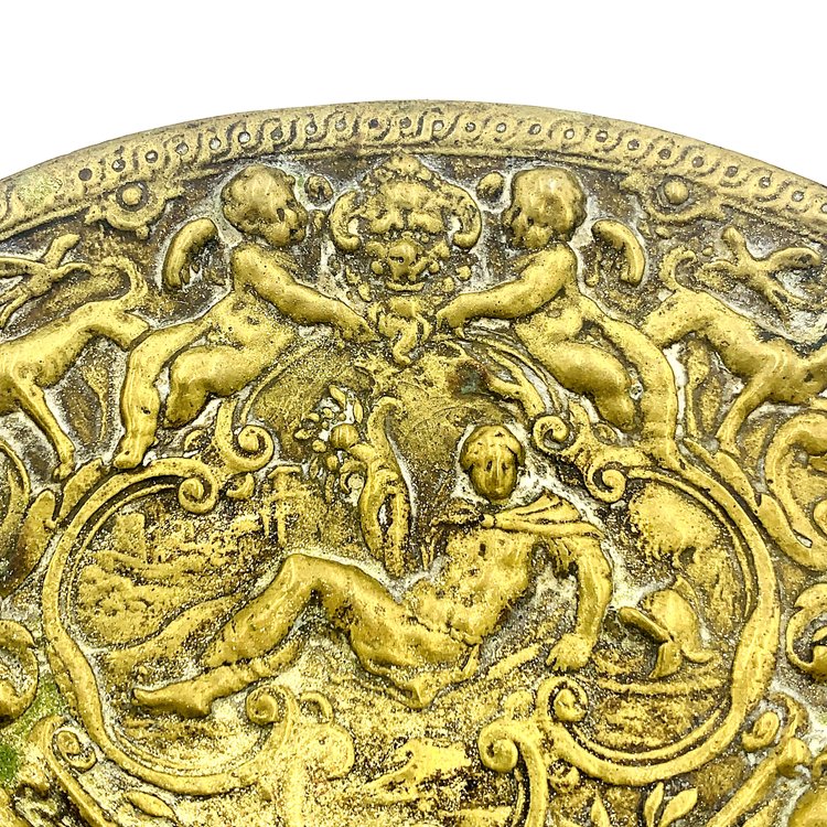 A brass candle holder from TAKAYASATO.COM with a scene of people and animals.