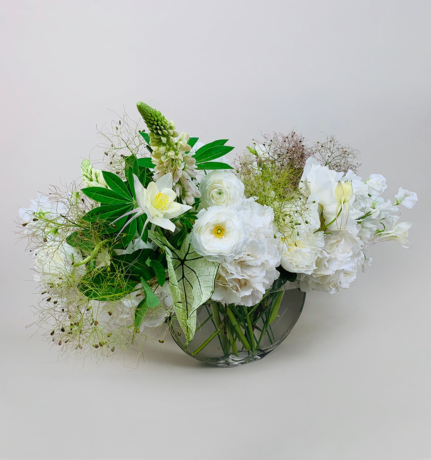 A beautiful arrangement of White, Green & Herbs flowers in a glass vase brightens up the table