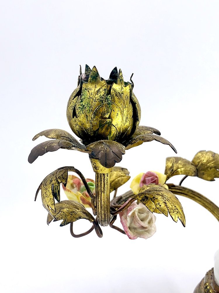 A gold candle holder with a flower on it. 
Product Name: Candle holder. Angels with bird. Porcelain and brass.
Brand Name: TAKAYASATO.COM