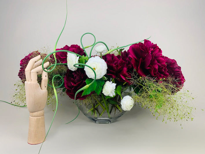 An arrangement of COLORFUL flowers in a vase next to a wooden mannequin from TAKAYASATO.COM.