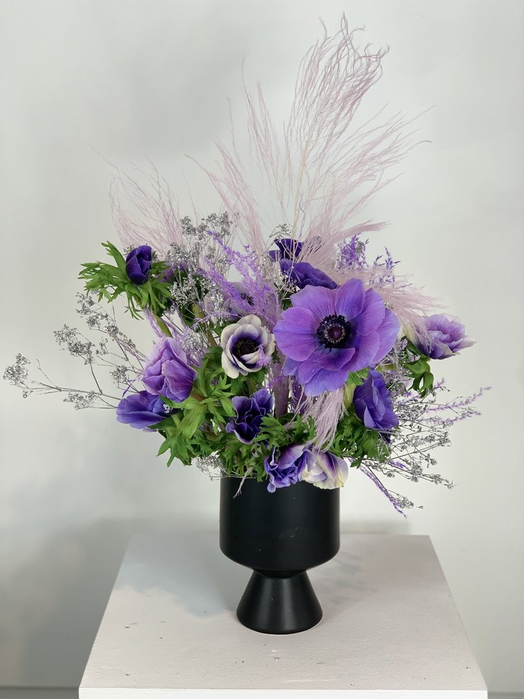 Purple MONOFLOWER in a modern black vase on a table by TAKAYASATO.COM.