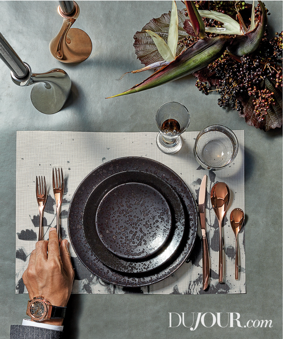 A table setting with a hand holding a knife and fork.