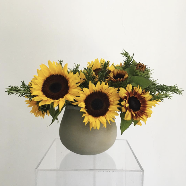 A MONOFLOWER vase of sunflowers on a clear stand exudes modern sophistication by TAKAYASATO.COM.