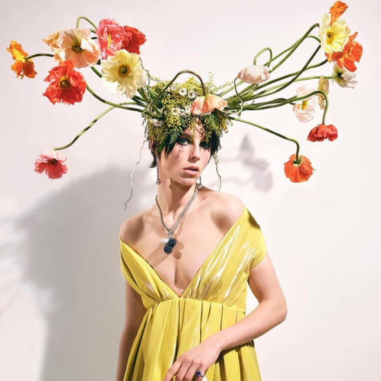 A woman in a yellow dress with abstract red and orange flowers on her head.
