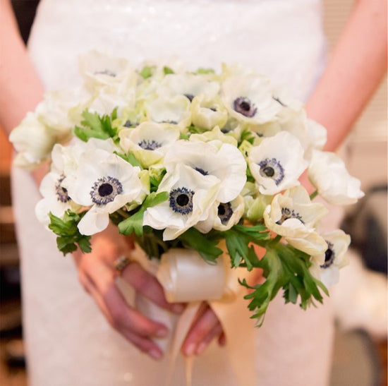A bride holds a bouquet of white anemones.