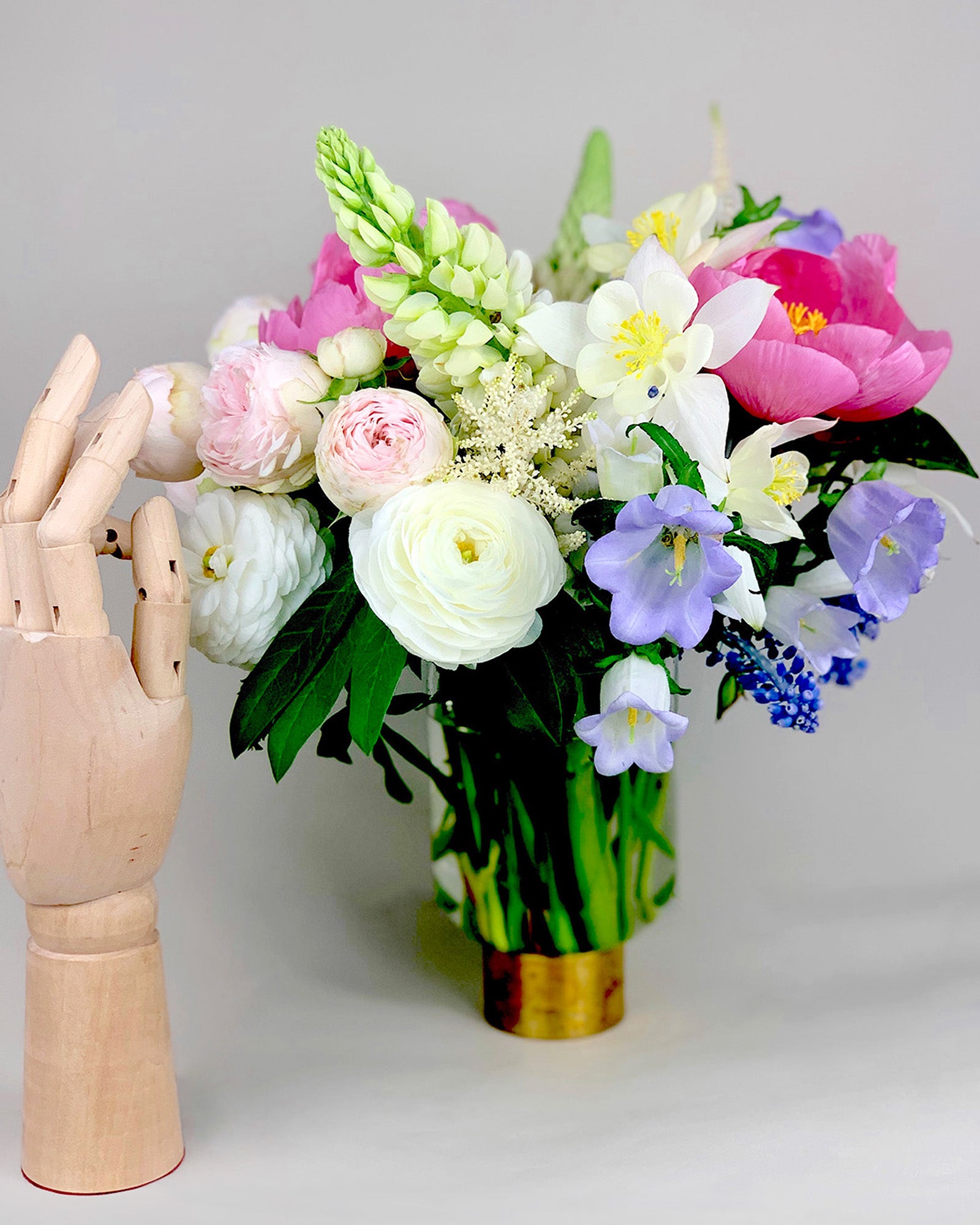 A vase of COLORFUL flowers next to a wooden mannequin by TAKAYASATO.COM creates a charming display.