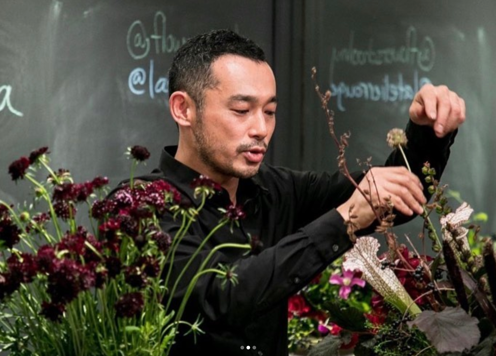 A master floral artist explaining how to make an arrangement to a class.