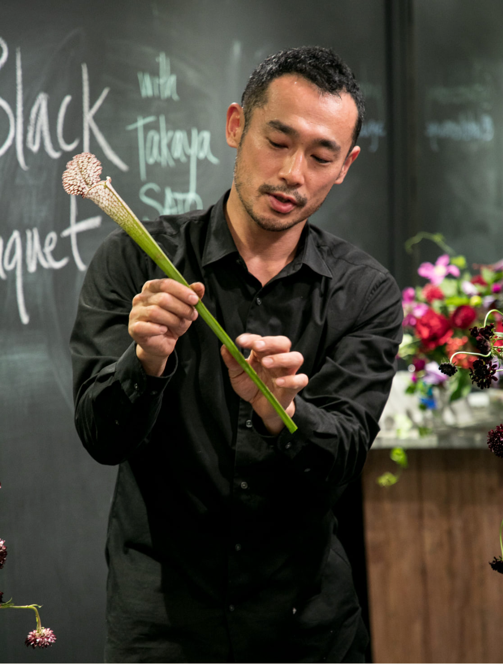 Takaya Sato holding a flower stem to show students how to arrange it in a vase.