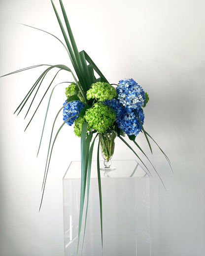 An eccentric flower arrangement inspired by the Charleston area, featuring blue and white hydrangea flowers and large palm fronds.