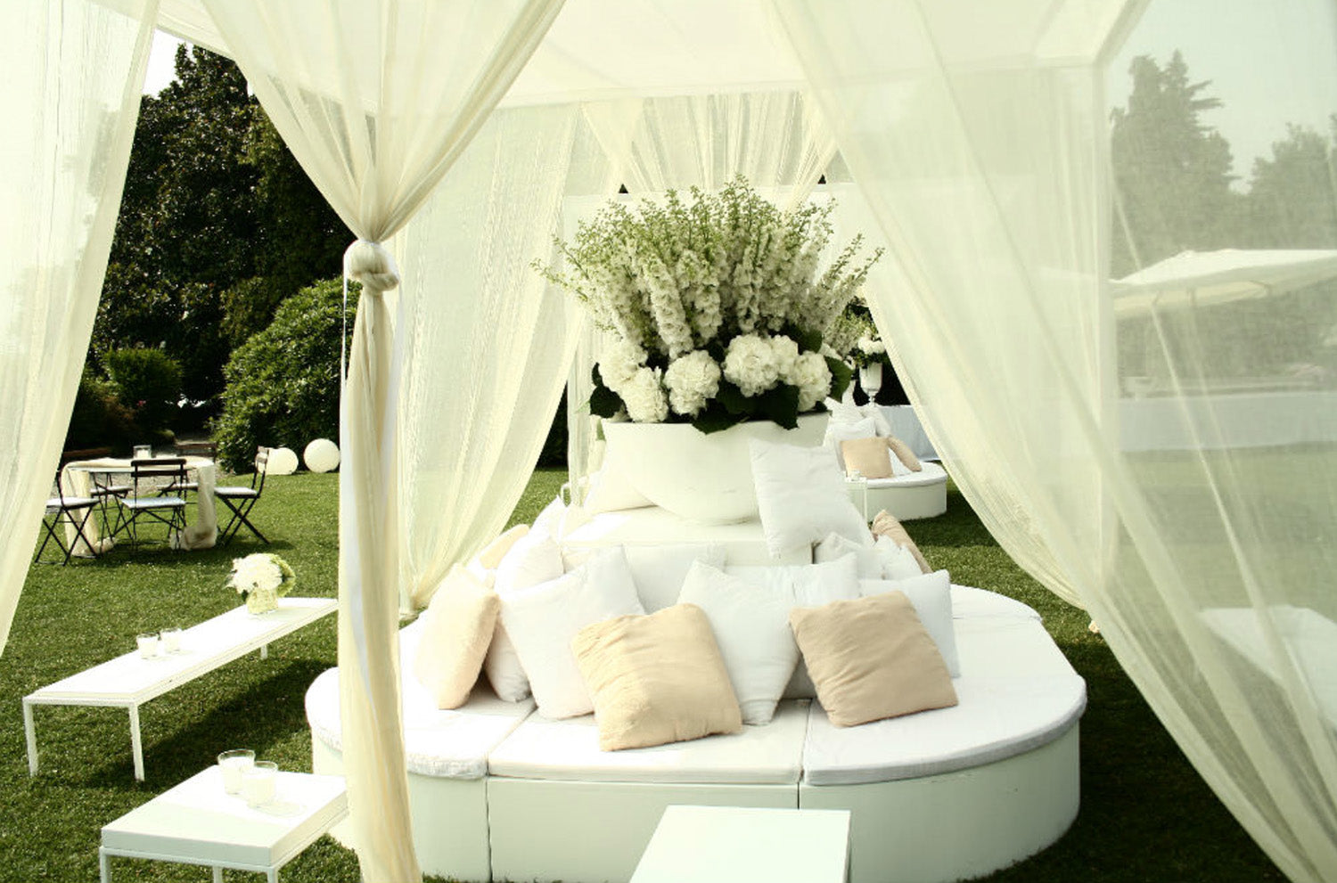 A white wedding tent with white pillows and white flowers.