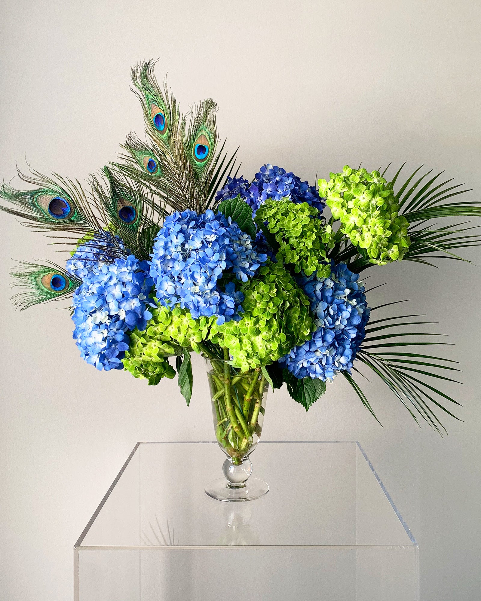 A lowcountry elegance flower arrangement featuring hydrangeas, palm leaves and peacock feathers