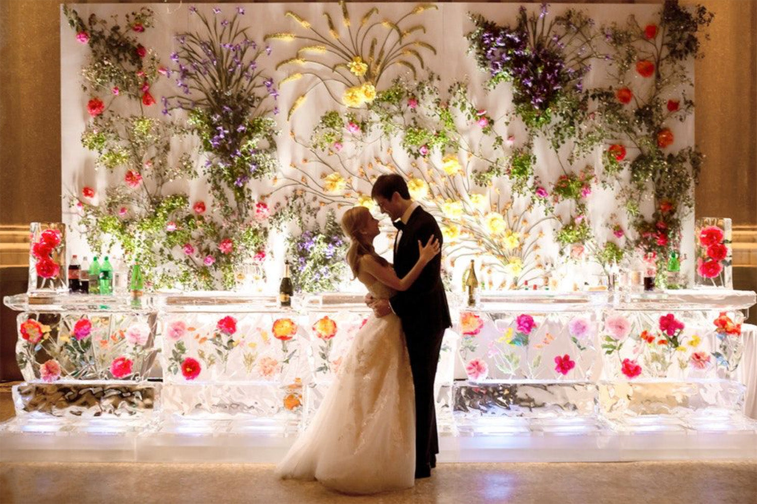 A bride and groom kiss in front of a luxurious floral backdrop.