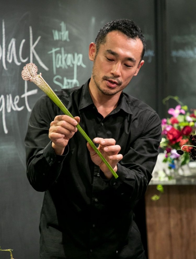 A man holding a bouquet of flowers in front of a chalkboard.
